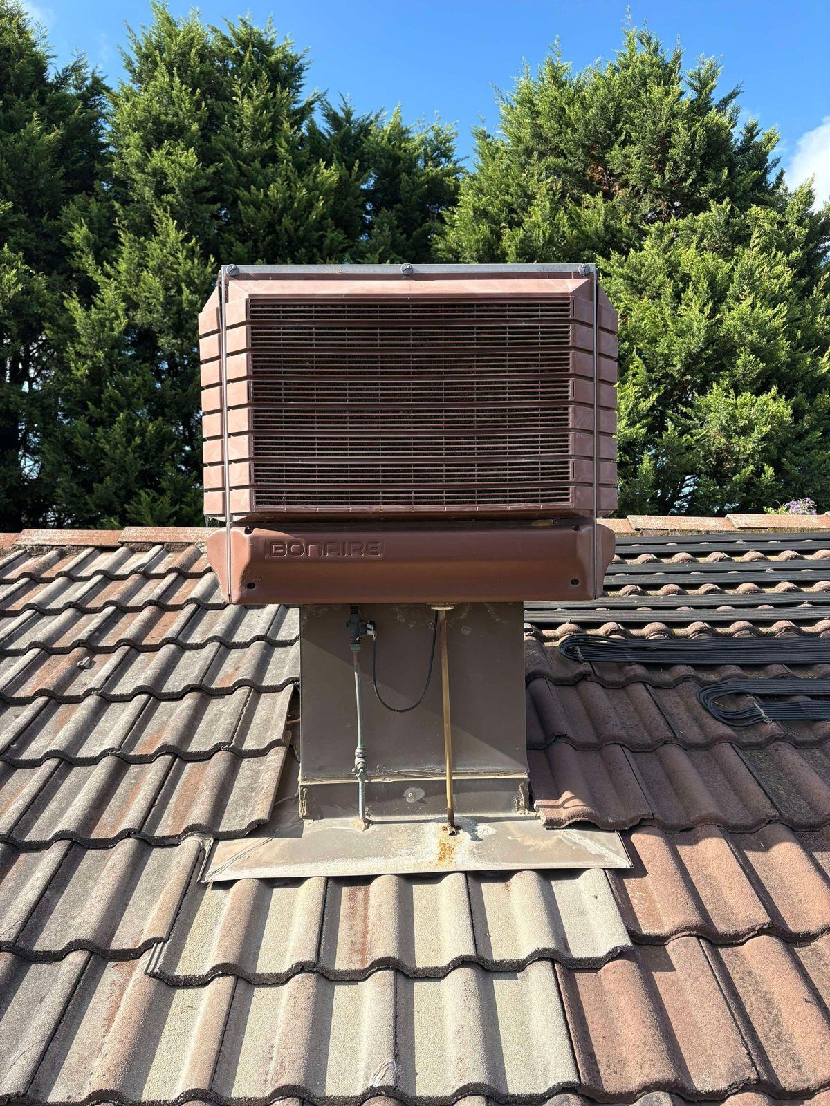 Evaporative cooler on a tiled roof with trees behind
